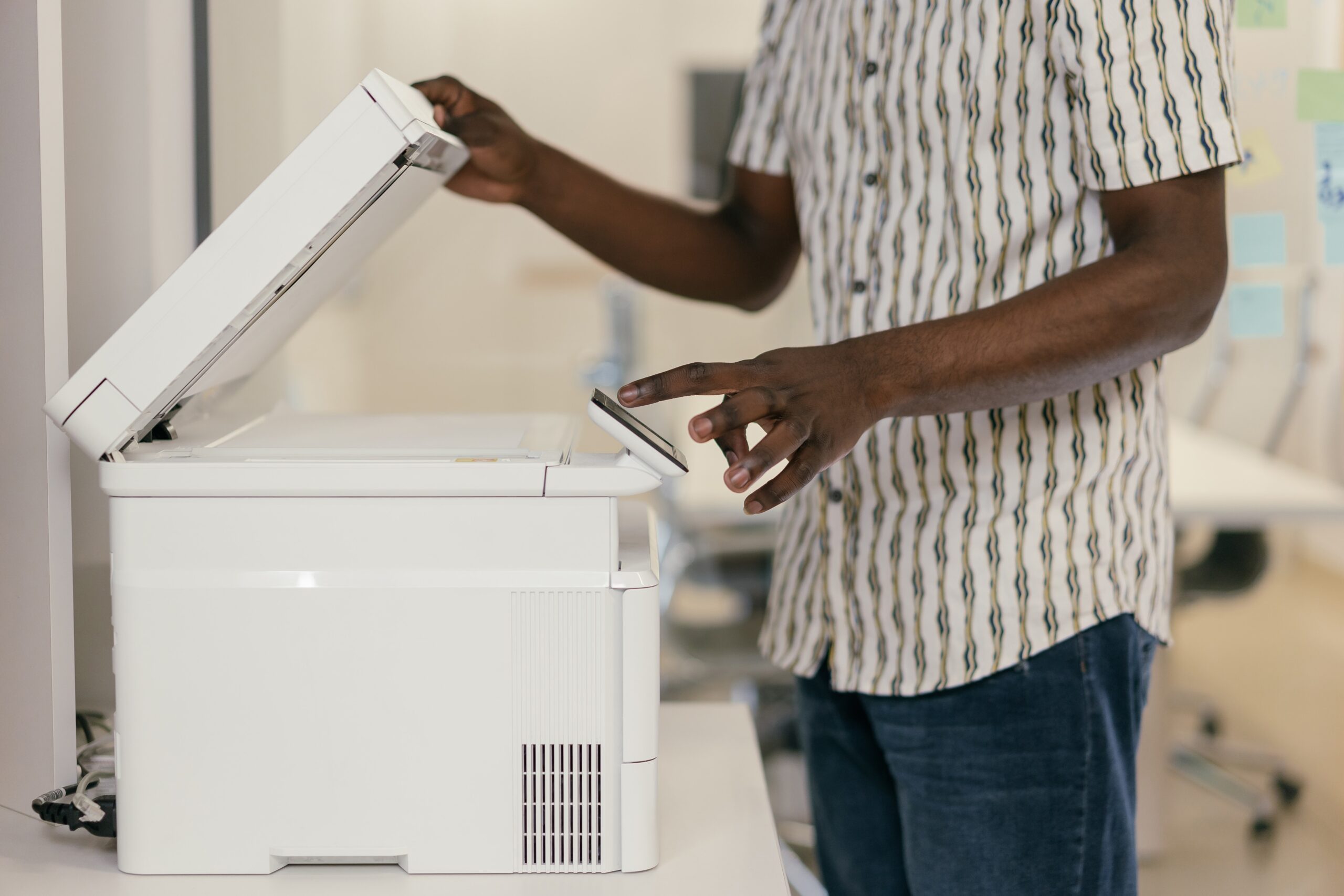 Person wearing a white and grey patterned shirt using white office printer/scanner, shown from torso down