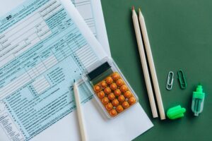 Photo of a tax form, calculator and pencils and green highlighter on a dark green desktop